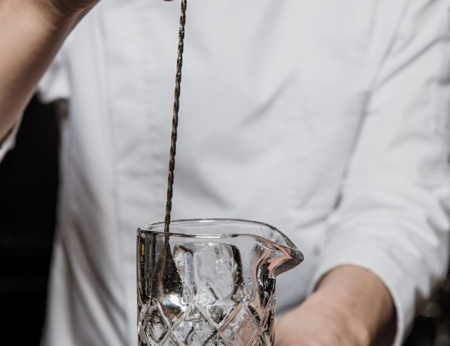 Bartender prepairing a cocktail at the bar stirring a drink in a mixing glass with a bar spoon